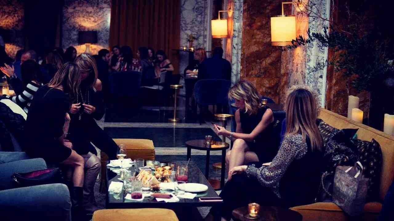 Salone bar con giovani seduti in oltrona che prendono un aperitivo